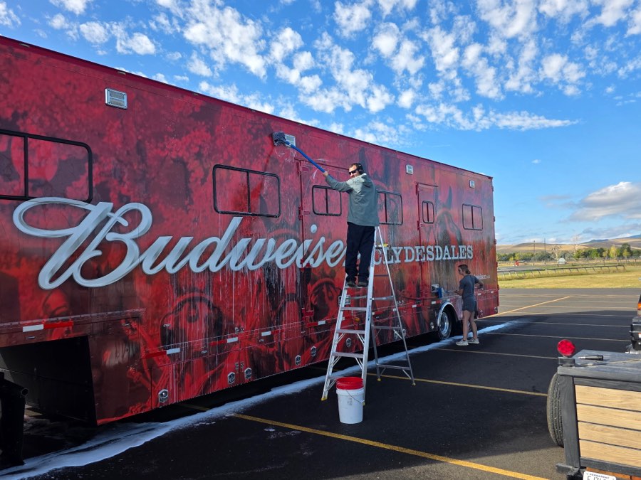 Velocity Racing crew hand-washing the side of a Budweiser Clydesdales trailer from a ladder